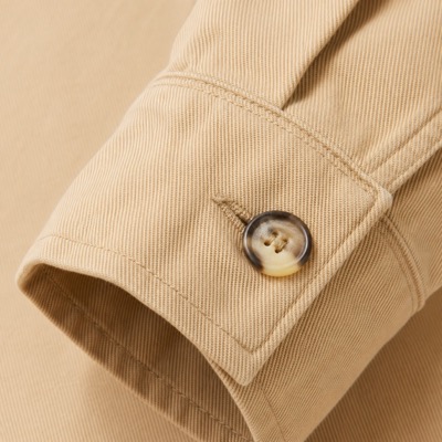 Close-up of sand-coloured cotton twill showing the weave texture and a horn button on the cuff